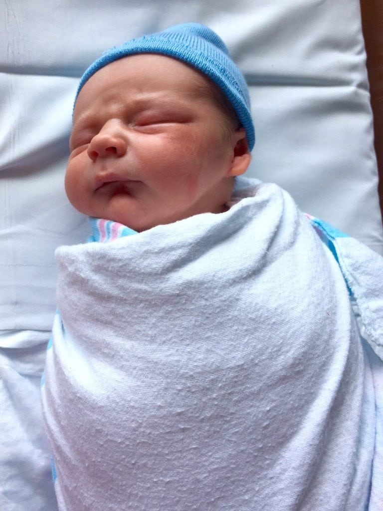 This newborn baby is adorable with his blue hat and blanket.