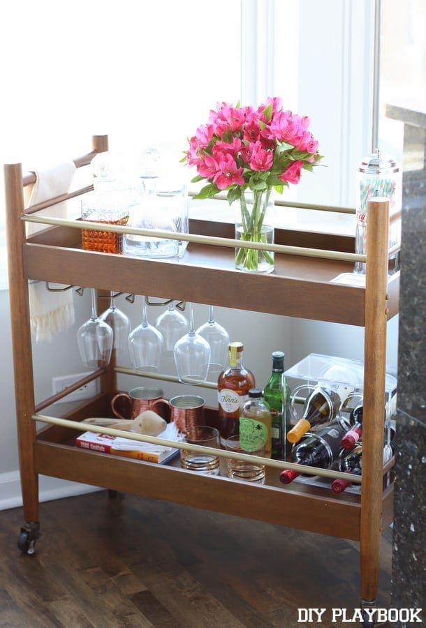 This elegant bar cart features fancy glassware and fresh pink flowers. 