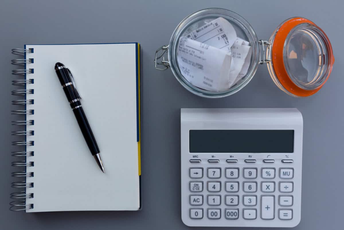 notebook with pen, calculate and glass jar used to store receipts