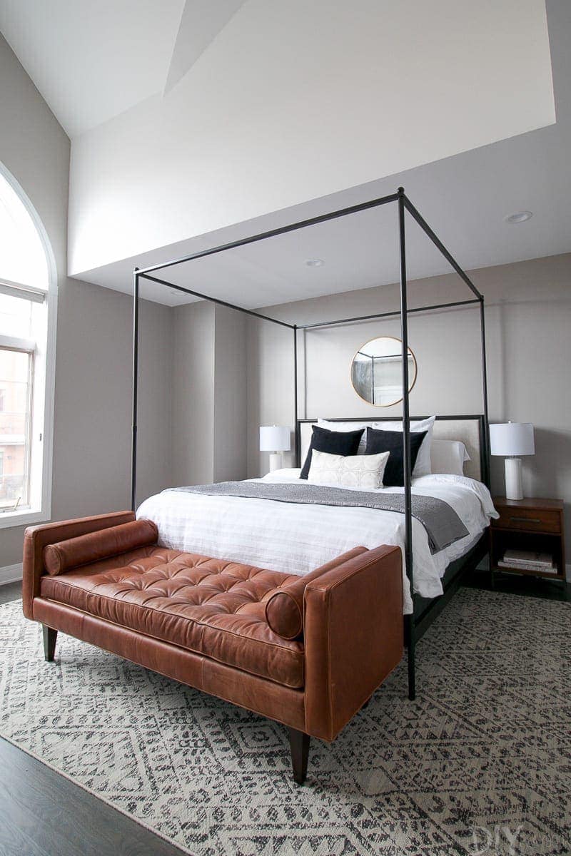 Master bedroom design with large bed and modern cube bed frame, brown leather bench and gray color scheme. 