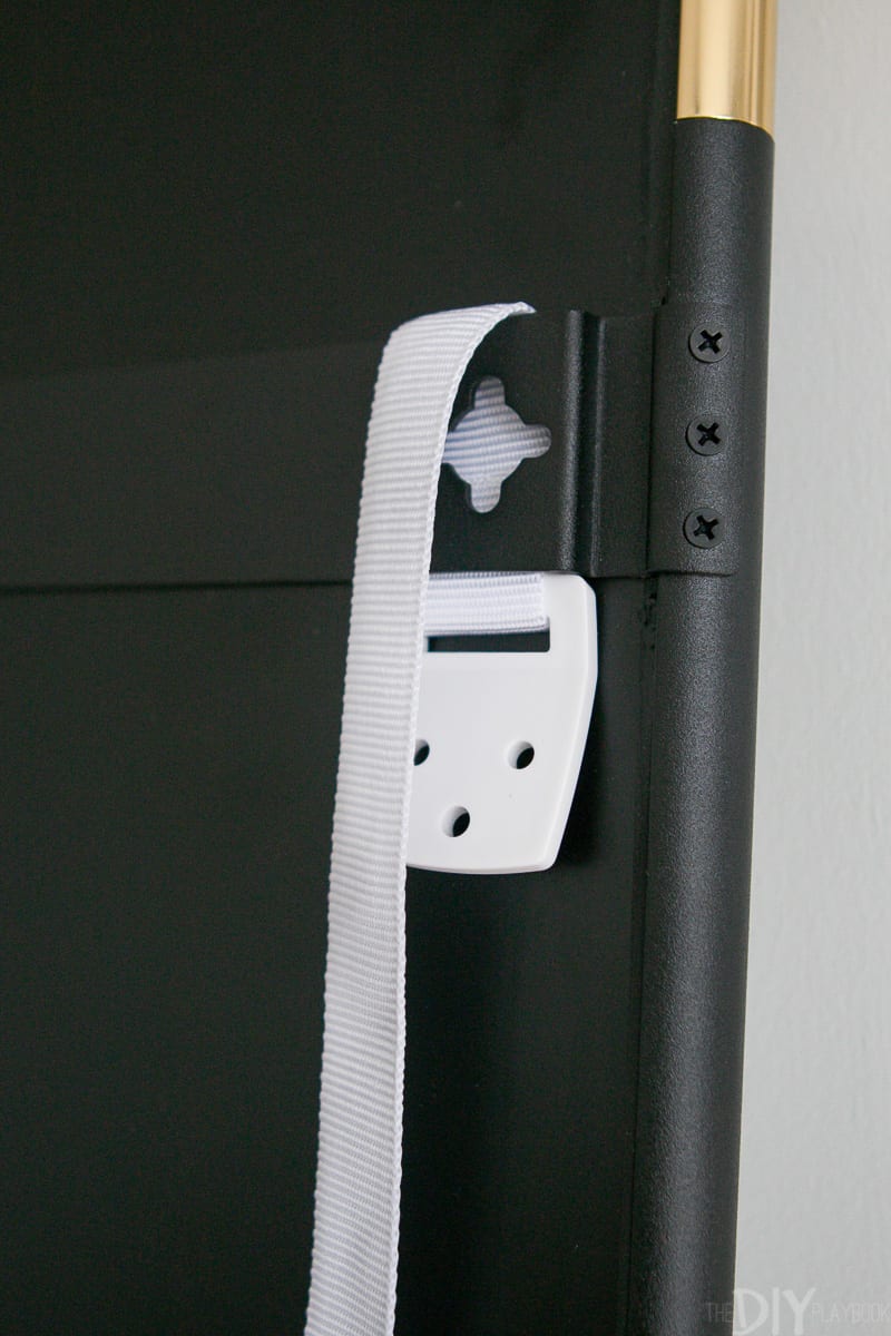 Sliding a furniture strap through the backside of a black metal mirror.