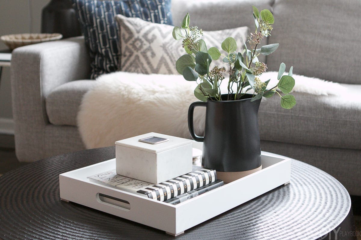 This black pitcher with faux eucalyptus is a great addition of color to this coffee table surface.