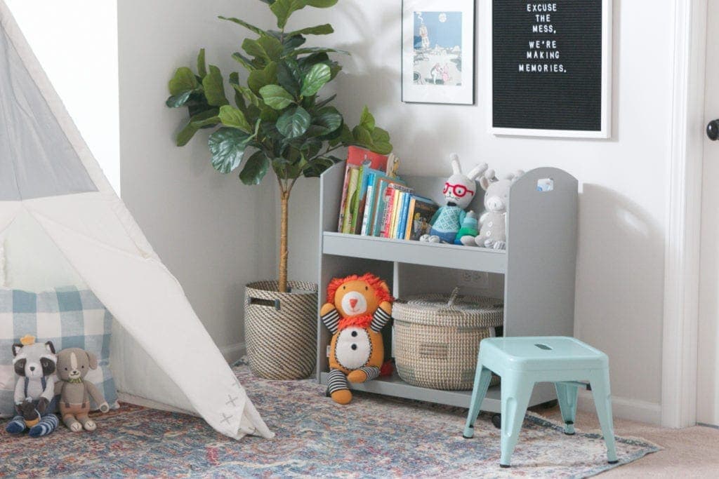 A faux fiddle leaf, bookcase on wheels, and teepee make up a play area