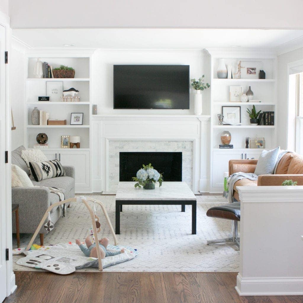 This neutral living room with a marble fireplace and white built-ins still has some work to do