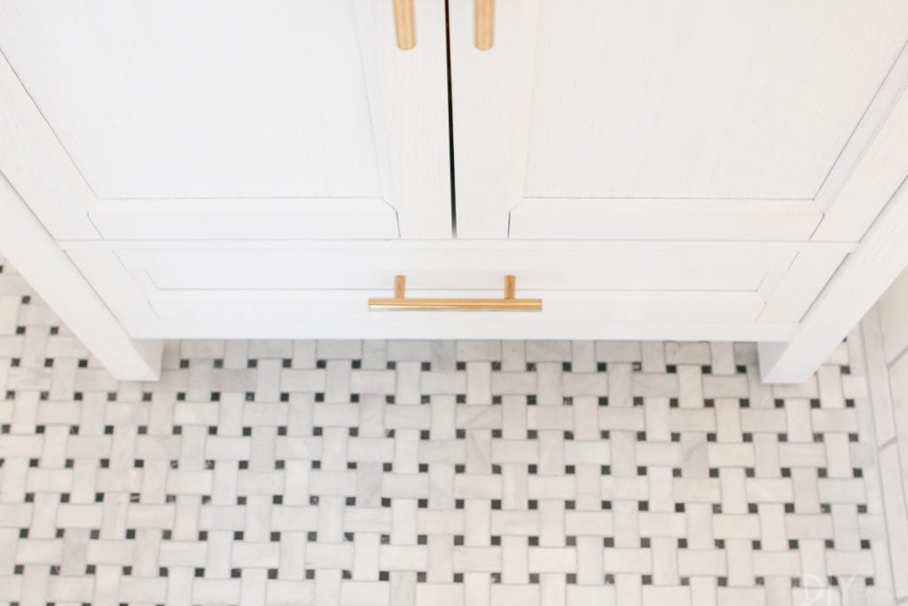 Marble basketweave floor tile with a white vanity and gold hardware