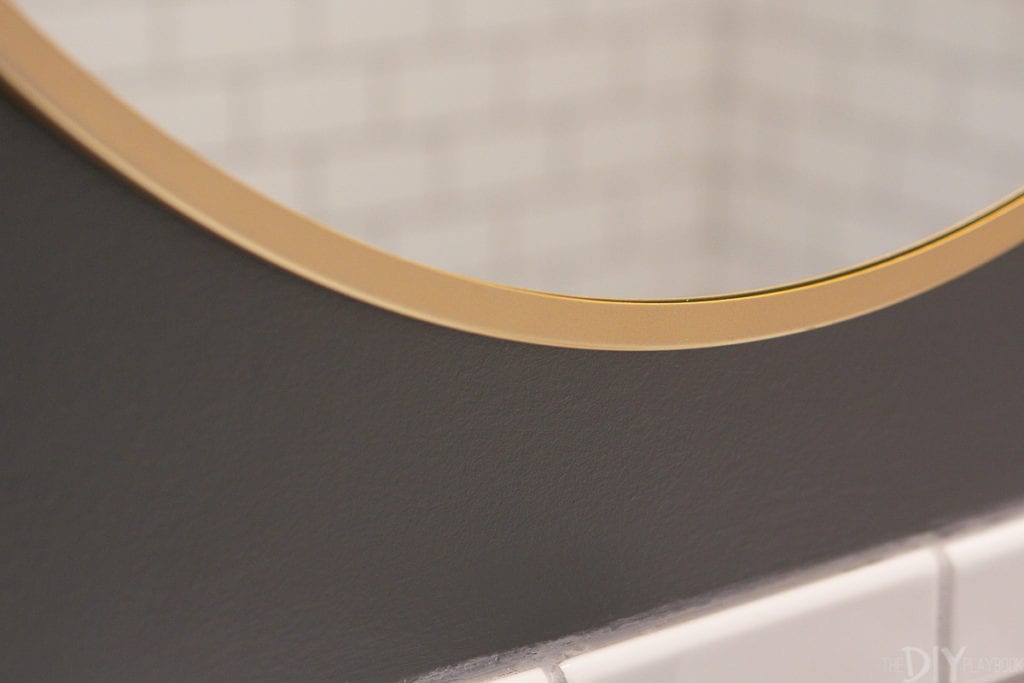 I love this round gold mirror next to the white subway tile and dark gray paint