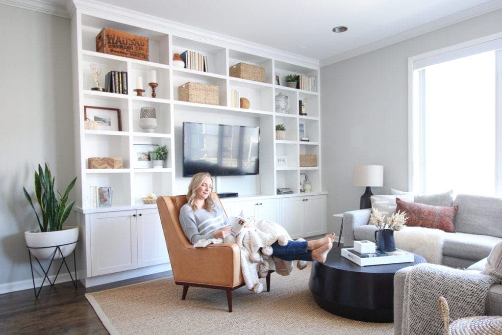 Reading in a living room with built ins and plants