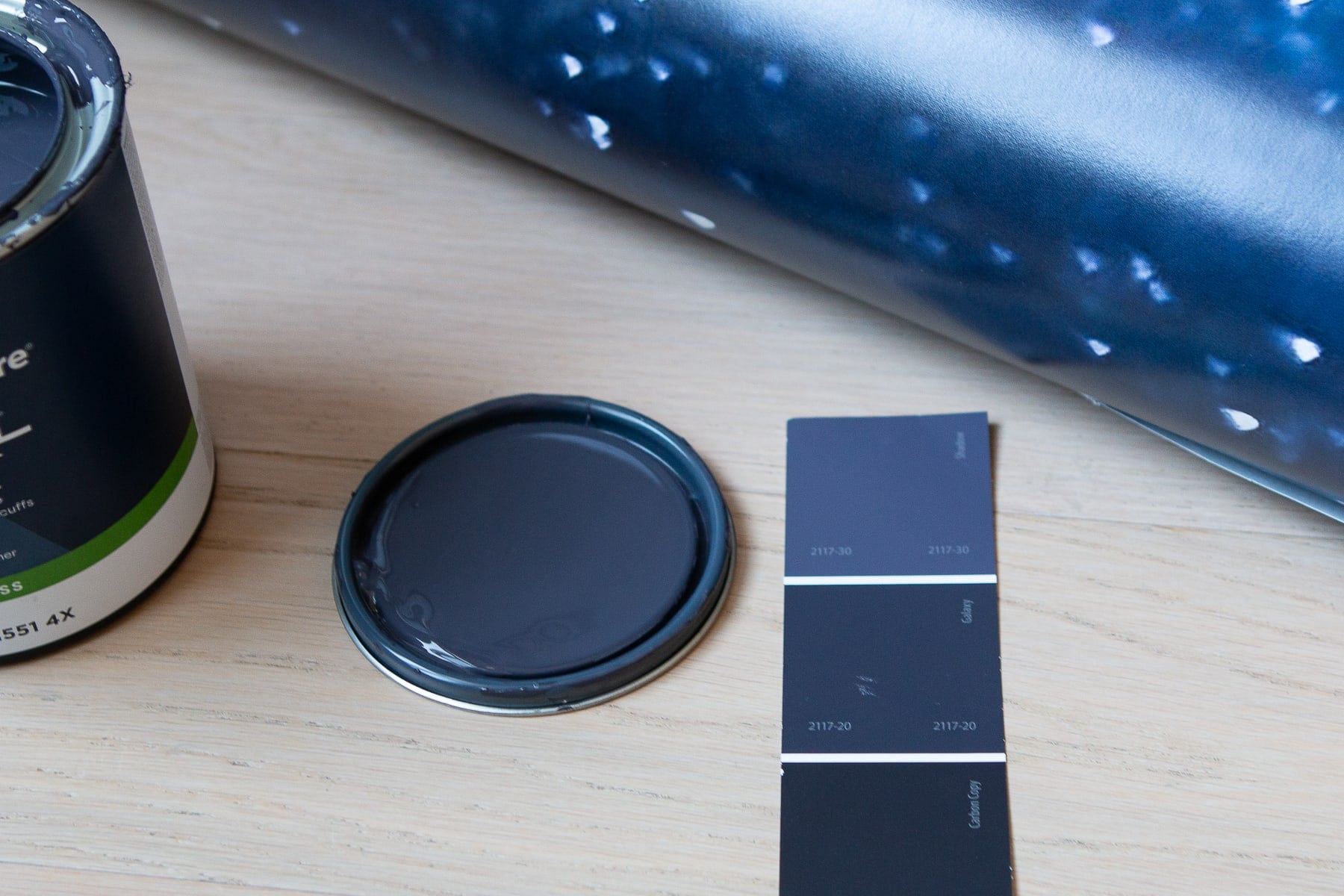 Blue paint color swatch next to a galaxy wallpaper and paint can lid with navy paint