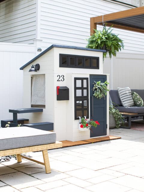 A backyard playhouse with a blue front door, flowers, and painted siding