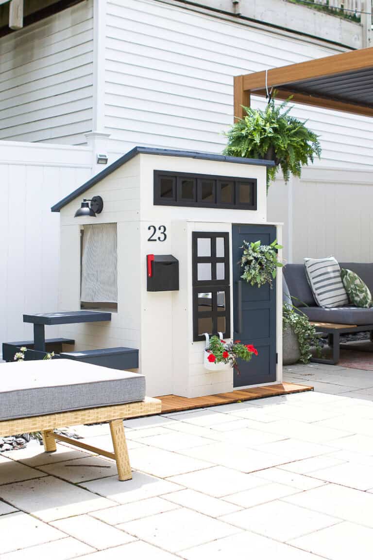 A backyard playhouse with a blue front door, flowers, and painted siding